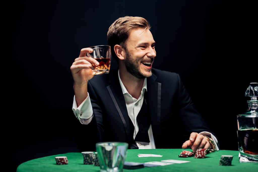 вибірковий фокус усміхненого чоловіка, що тримає скло з алкоголем ізольовано на чорному
  - Фото, зображення