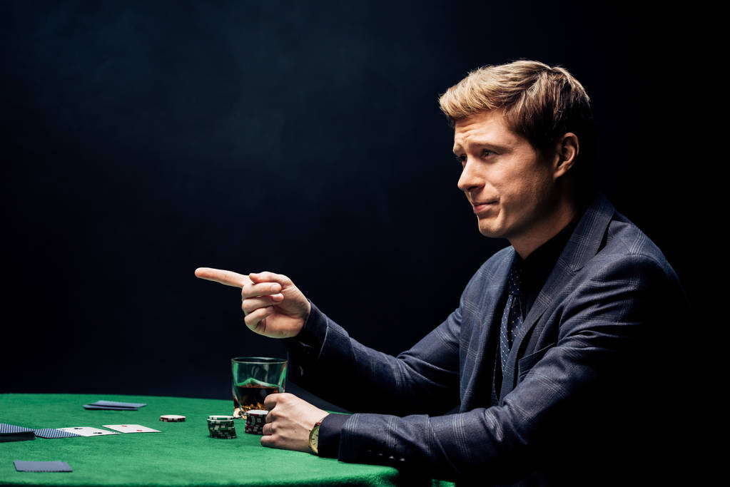 pohledný muž, ukazující prstem blízko pokrového stolu na černém  - Fotografie, Obrázek