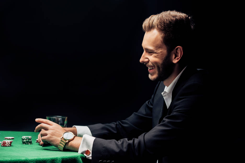 ευτυχισμένο μούσι άνθρωπος χαμογελά κοντά στο τραπέζι πόκερ απομονώθηκε σε μαύρο  - Φωτογραφία, εικόνα