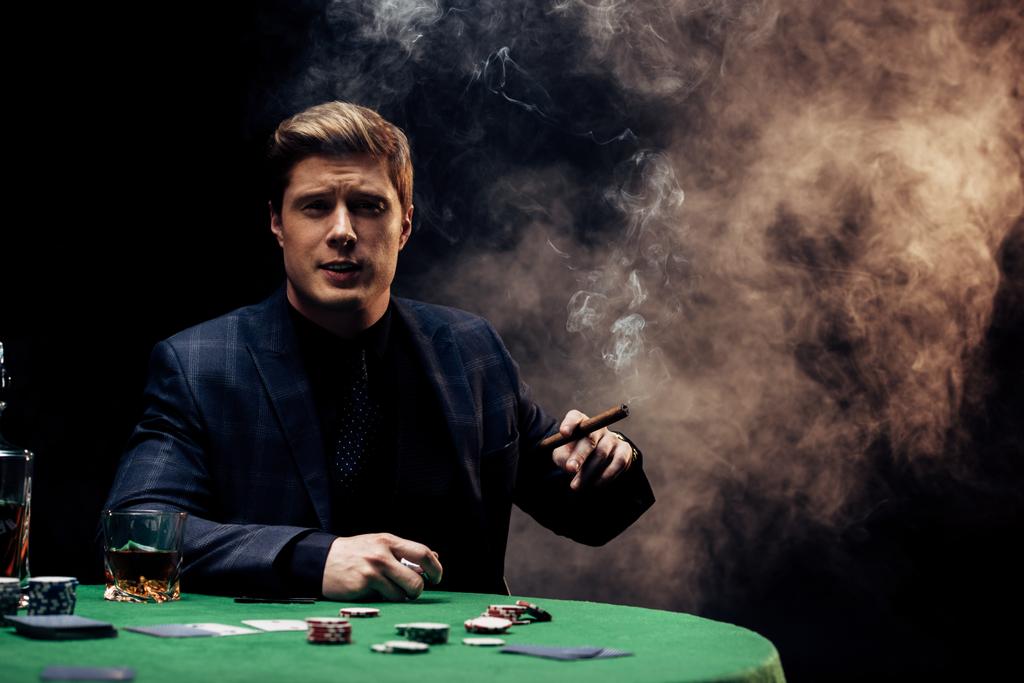 schöner Mann mit Zigarre beim Rauchen auf schwarz mit Rauch  - Foto, Bild