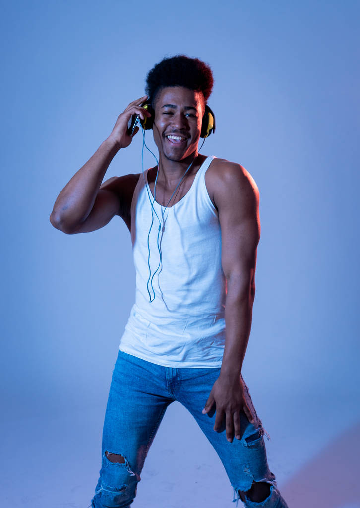 Сильный африканский юный танцор слушает музыку в интернете, танцует и поет в наушниках. Художественный портрет с диско танцполом неоновый свет в Интернет Музыкально-технологическая концепция
. - Фото, изображение