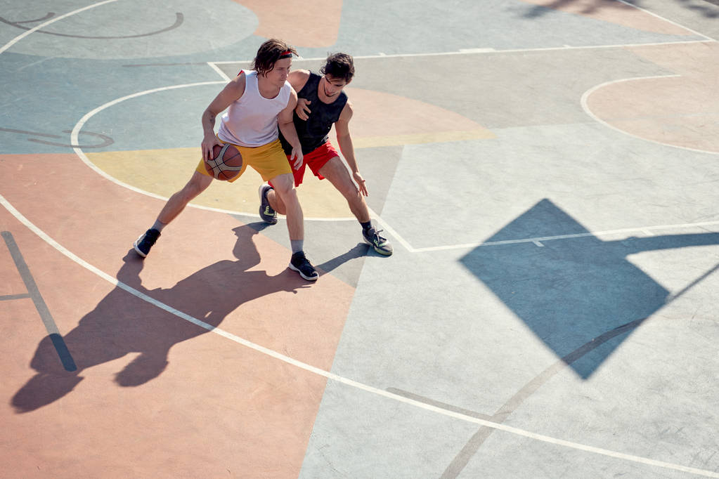 Widok z góry zdjęcie dwóch sportowców mężczyzn gra w koszykówkę na placu zabaw w godzinach porannych. - Zdjęcie, obraz
