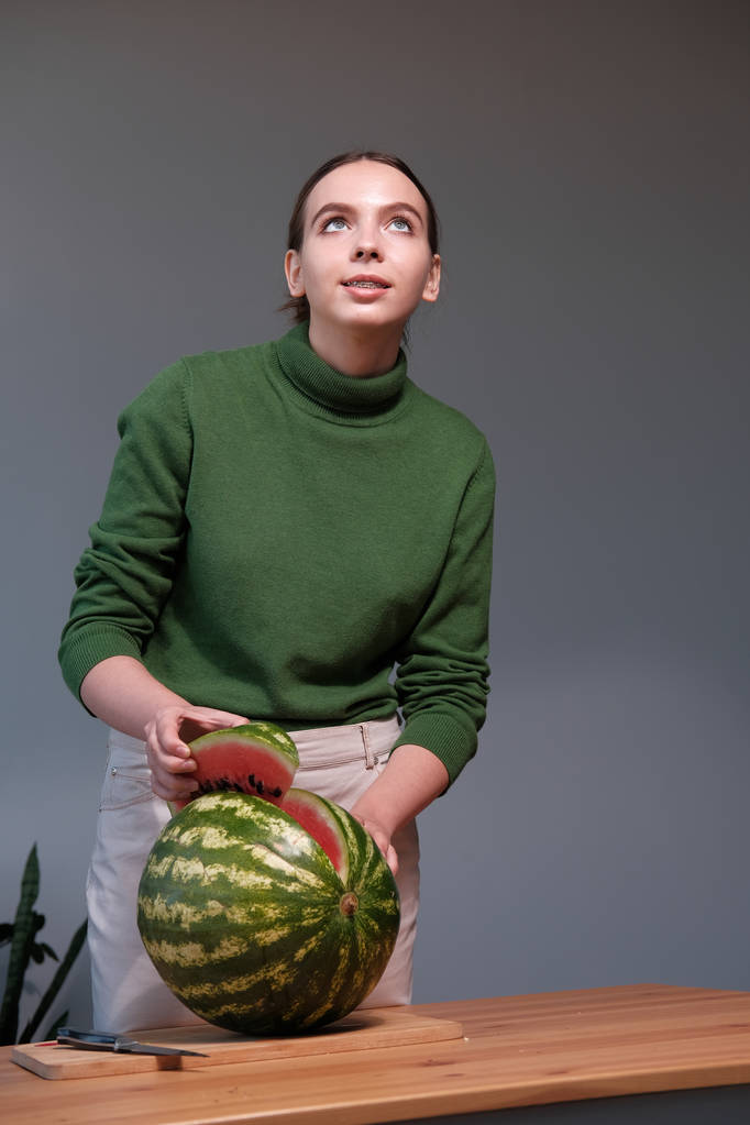 jonge vrouw snijden rijpe watermeloen in huis interieur - Foto, afbeelding