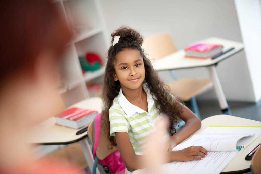 Красивая темнокожая девушка сидит за столом во время урока
 - Фото, изображение
