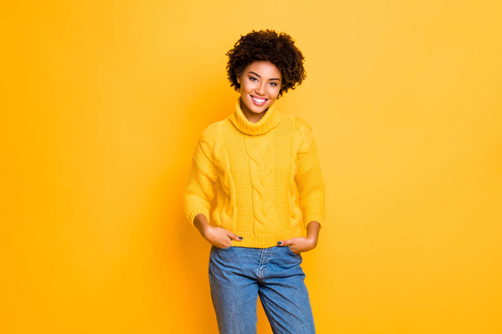 良い気分で暗い肌の面白い女性の写真は暖かいニットプルオーバーとジーンズを着用孤立した黄色の背景を立って - 写真・画像