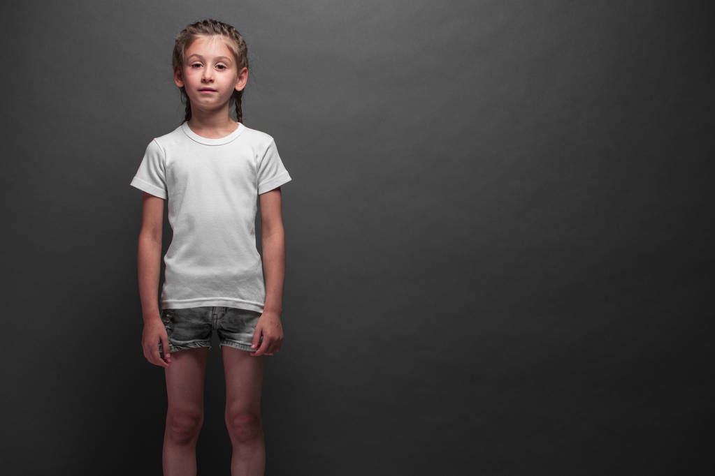 白いTシャツを着た子供の女の子は、あなたのロゴやグレーの背景の上にデザインのためのスペースを持つ - 写真・画像