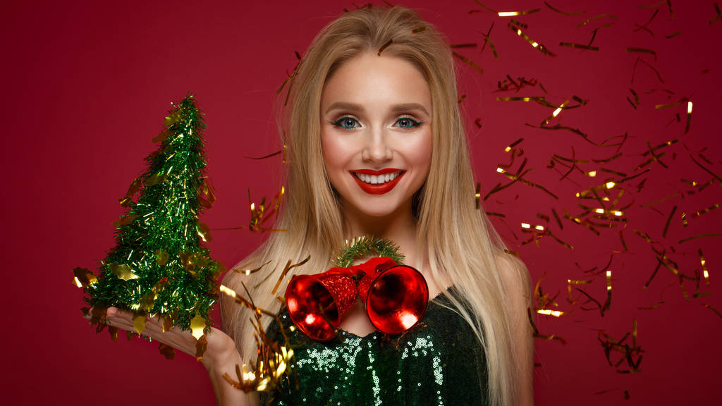 Bella ragazza bionda in un'immagine di Capodanno con campane di Natale intorno al collo e albero verde. Bellezza viso con trucco festivo
. - Foto, immagini