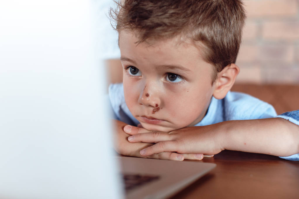 Niño rubio lindo mirando atentamente a la pantalla del ordenador portátil. Niños y tecnología
 - Foto, imagen