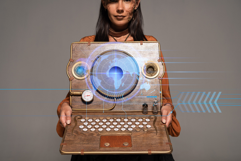 cropped view of steampunk woman in top hat with goggles showing vintage laptop with digital map isolated on grey - 写真・画像