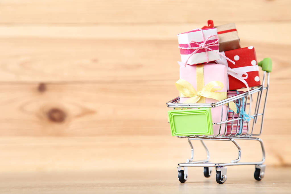 Small shopping cart with gift boxes on brown wooden table - Photo, Image