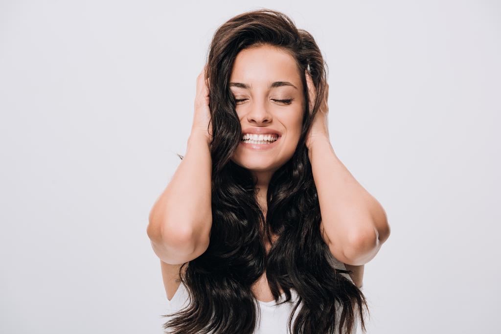 happy brunette beautiful woman touching long curly healthy hair isolated on grey - Photo, Image