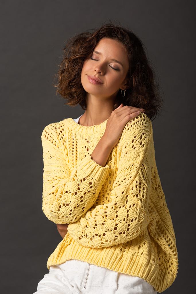 curly woman with closed eyes in yellow knitted sweater on black background - Photo, Image