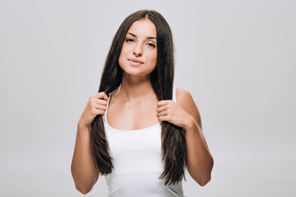 брюнетка красива жінка тримає довге пряме здорове і блискуче волосся ізольоване на сірому
 - Фото, зображення