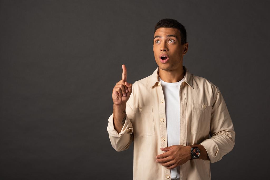 handsome mixed race man in beige shirt showing idea gesture on black background - Photo, Image