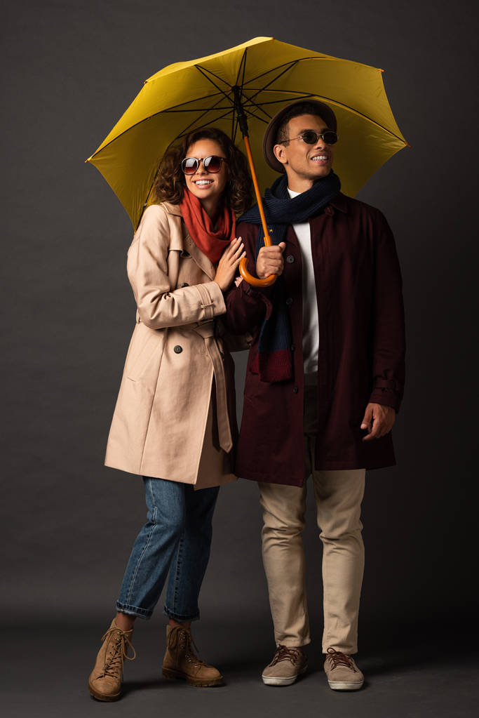 szczęśliwy stylowy Interracial para jesienią strój z żółtym parasolem na czarnym tle - Zdjęcie, obraz