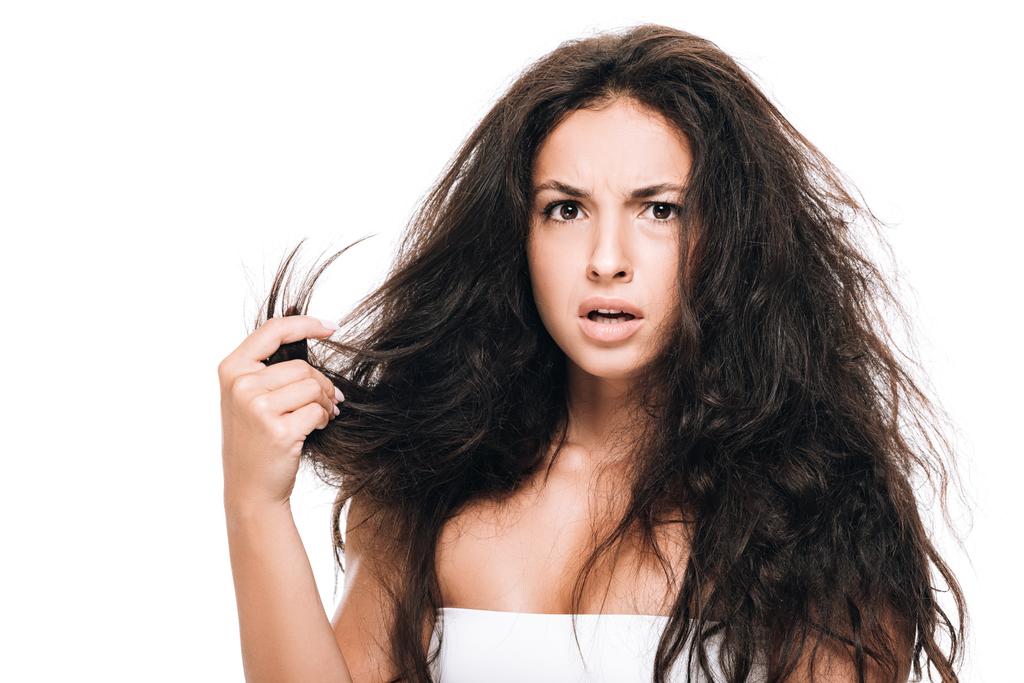 estresado morena hermosa mujer sosteniendo dañado cabello seco aislado en blanco
 - Foto, Imagen