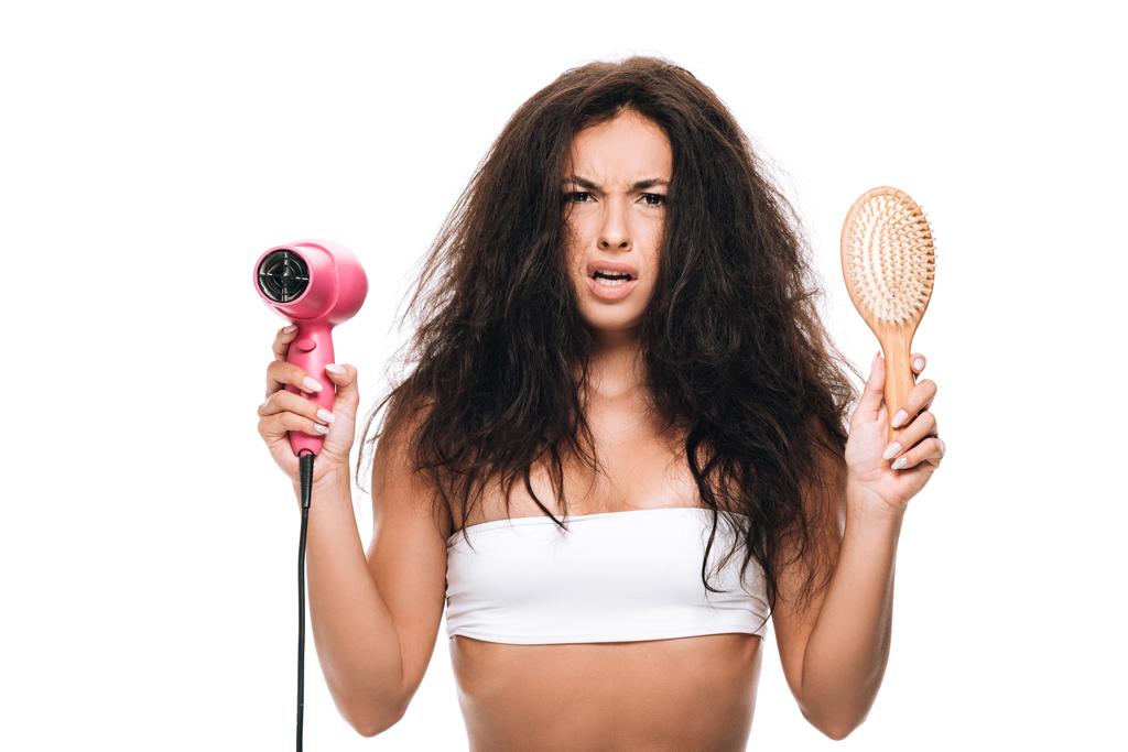 preoccupato bruna bella donna con i capelli ricci in possesso di asciugacapelli rosa e pettine isolato su bianco
 - Foto, immagini