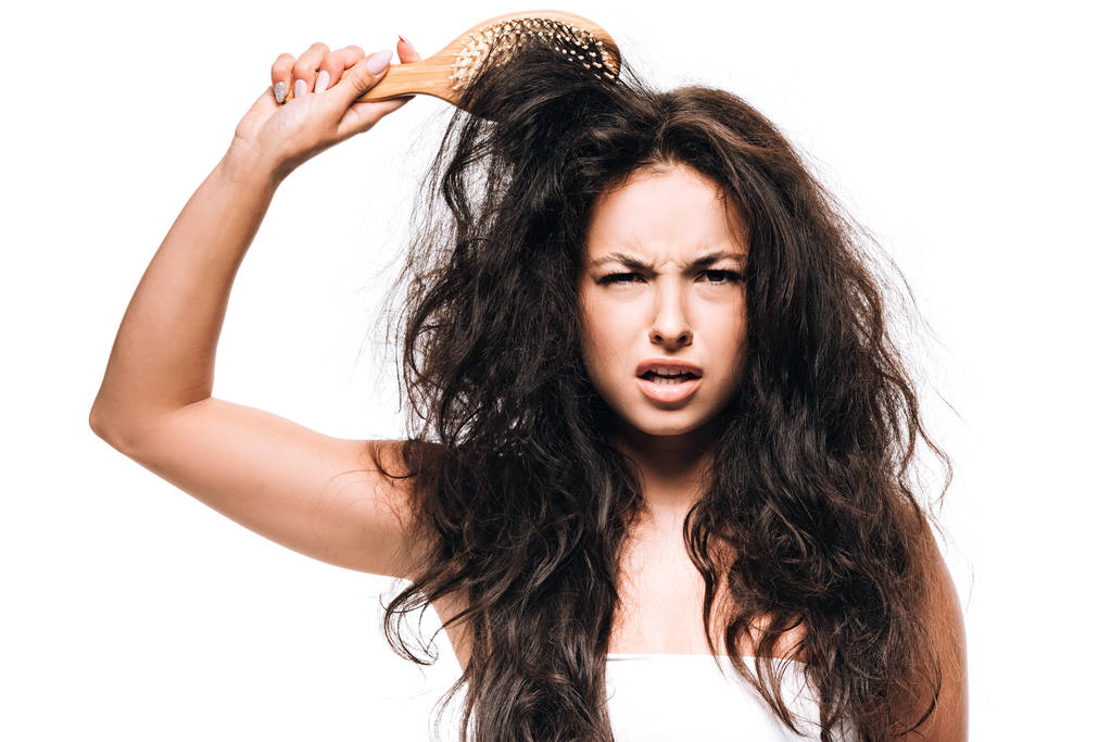 смущенная брюнетка с непослушными вьющимися волосами и расчёской, изолированной на белом
 - Фото, изображение
