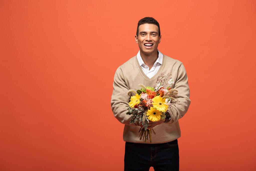 счастливый смешанной расы человек держит осенний букет изолирован на оранжевый
 - Фото, изображение