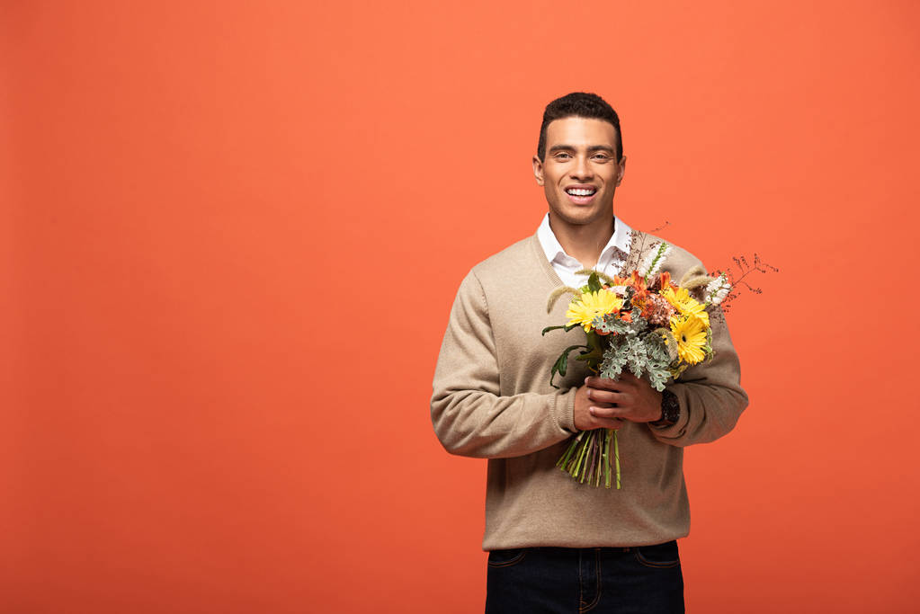 улыбающийся смешанная раса человек держит осенний букет изолирован на оранжевый
 - Фото, изображение