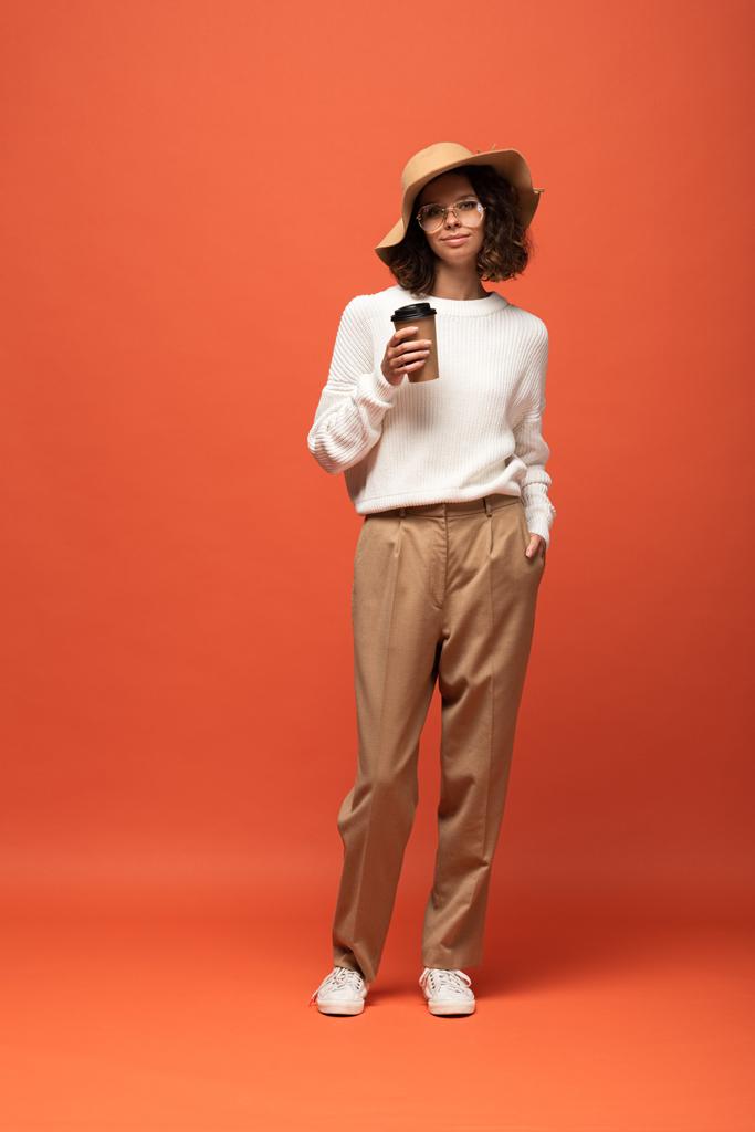 женщина в шляпе и очках, держащая кофе, чтобы пойти на апельсин
 - Фото, изображение