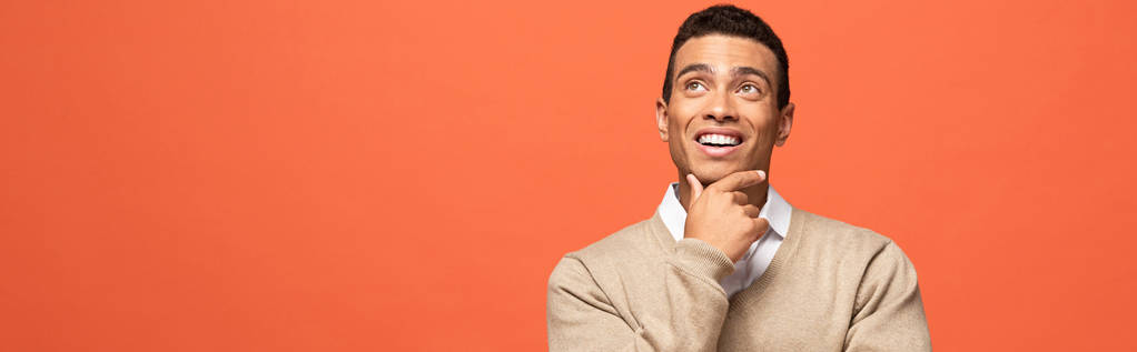 plano panorámico del hombre de raza mixta de ensueño en suéter beige mirando hacia otro lado aislado en naranja
 - Foto, imagen