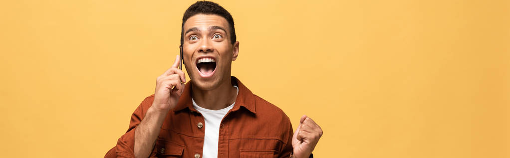 panoramatický záběr šťastného Smíšené rasy, která mluví na telefonu Smartphone a zobrazuje Ano gesto izolované na žlutém - Fotografie, Obrázek