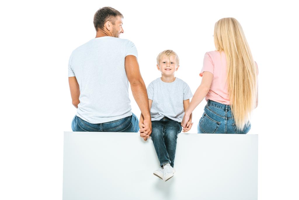 γονείς κάθονται σε κύβο και κρατώντας το χέρι με χαρούμενο γιο απομονώνονται σε λευκό  - Φωτογραφία, εικόνα