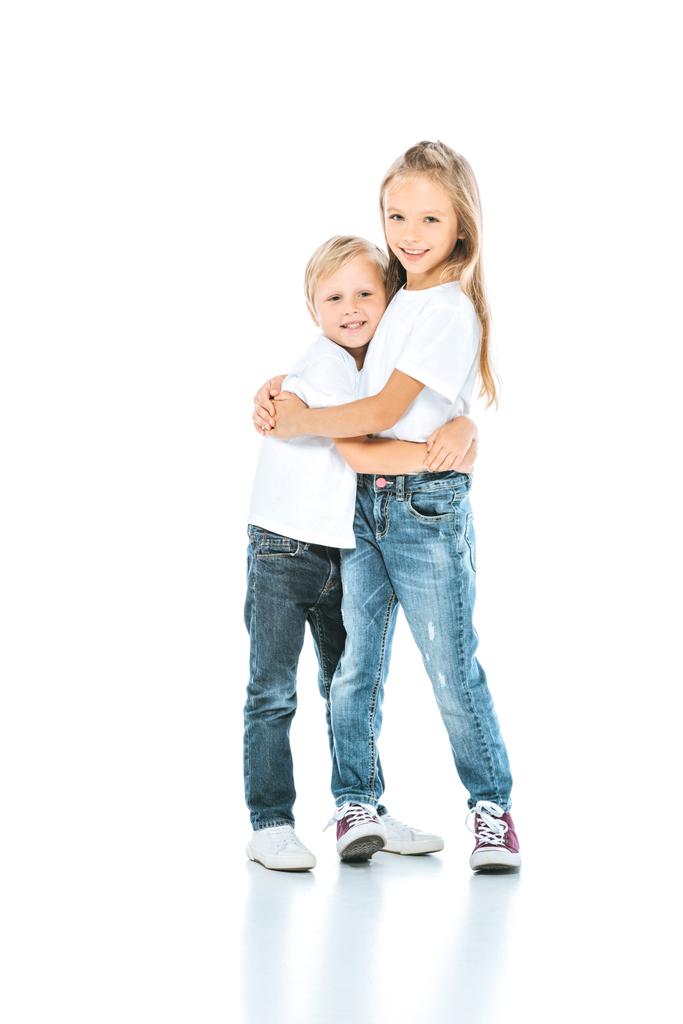 Ευτυχισμένο παιδί αγκαλιάζει χαρούμενο αδελφό, ενώ στέκεται σε λευκό - Φωτογραφία, εικόνα