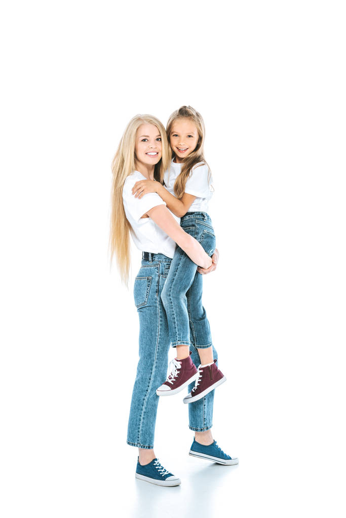 Ευτυχισμένη μητέρα που κρατάει αγκαλιά χαριτωμένη κόρη και στέκεται στα λευκά - Φωτογραφία, εικόνα