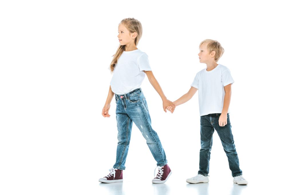 δύο χαριτωμένα παιδιά κρατώντας τα χέρια και περπατώντας στα λευκά  - Φωτογραφία, εικόνα
