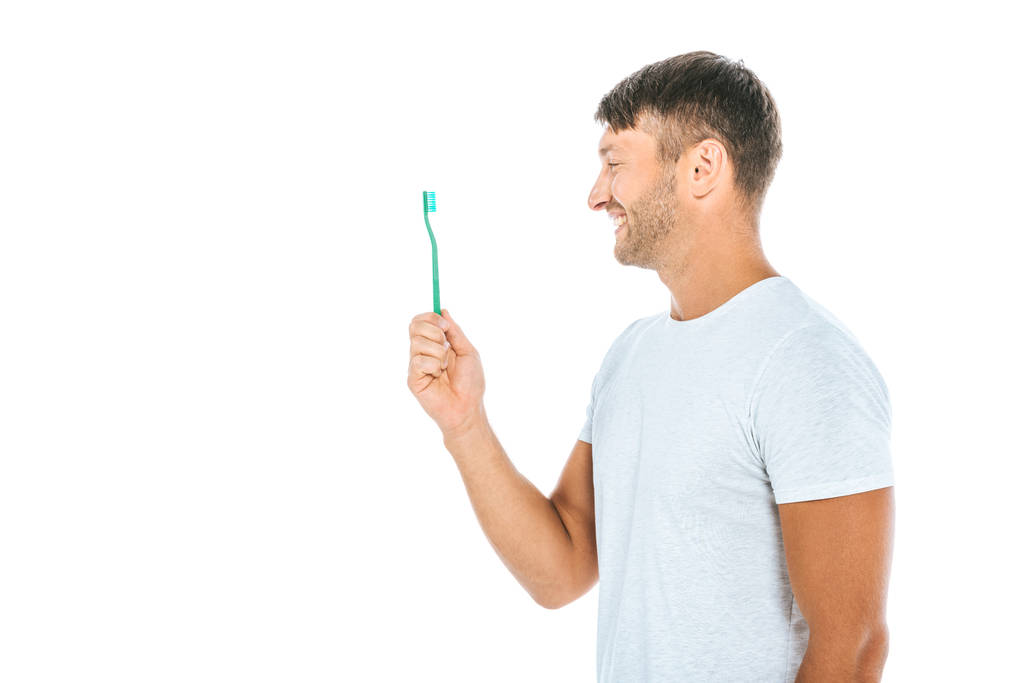 歯ブラシを見ている陽気な男の横で白に隔離された笑顔  - 写真・画像