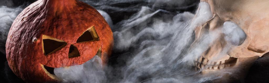 tiro panorâmico de assustador crânio humano e esculpida abóbora de Halloween no fundo preto
 - Foto, Imagem
