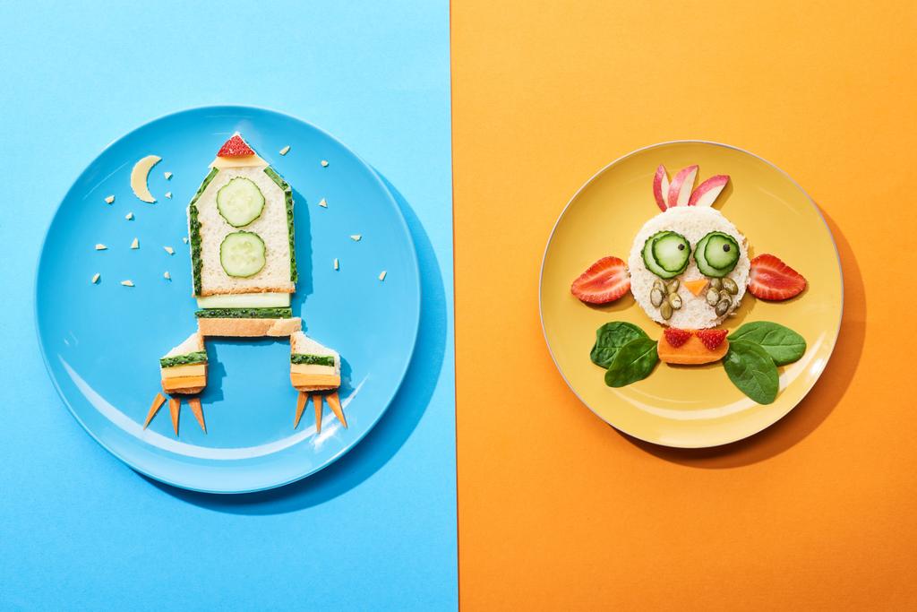 top view of plates with fancy face and rocket made of food for childrens breakfast on blue and orange background - Photo, Image