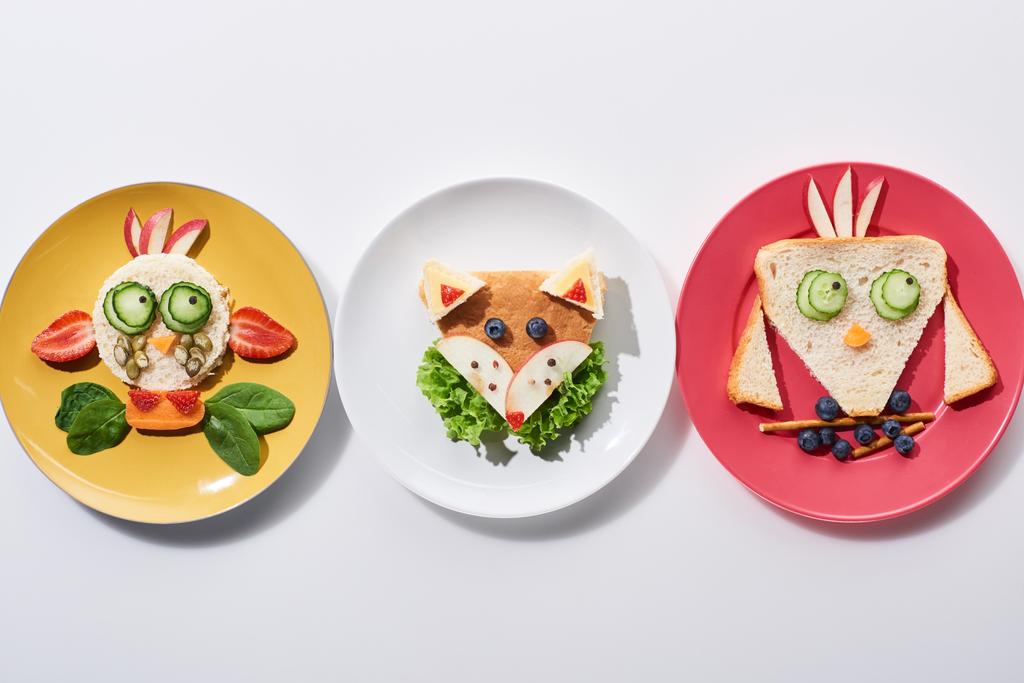 白い背景に子供の朝食のための食べ物で作られた派手な牛 鳥やキツネとプレートのトップビュー ロイヤリティフリー写真 画像素材