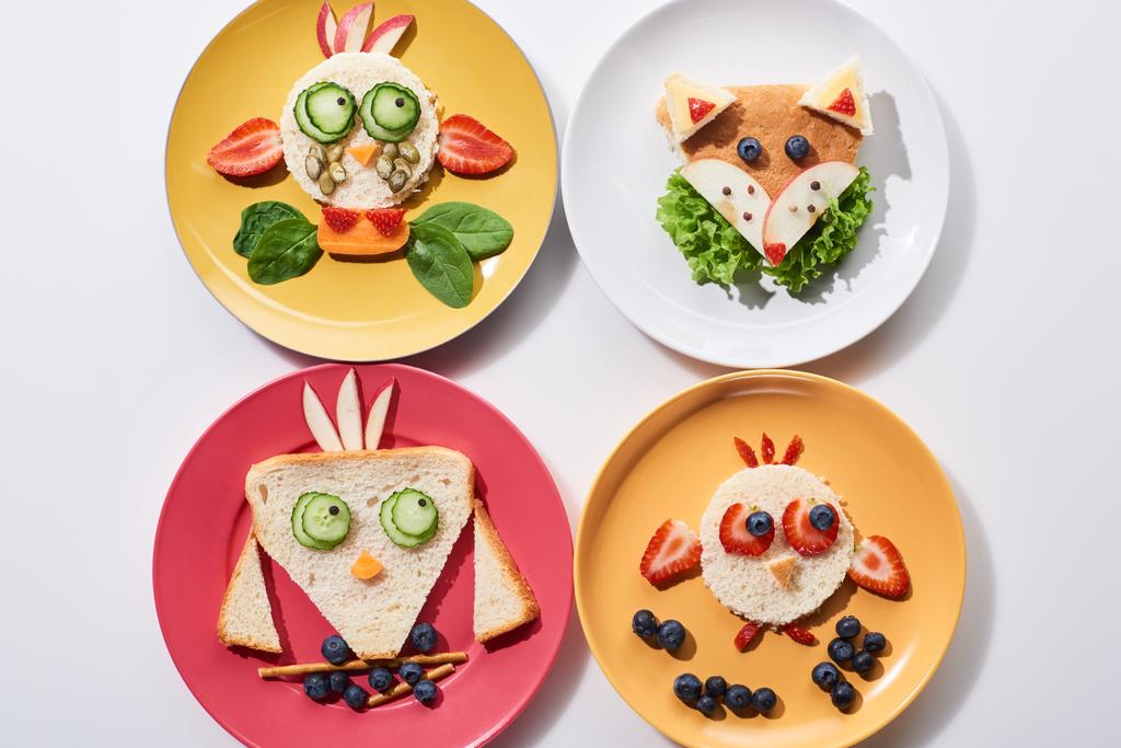 Teller mit ausgefallenen Tieren aus Futter für das Kinderfrühstück auf weißem Hintergrund - Foto, Bild