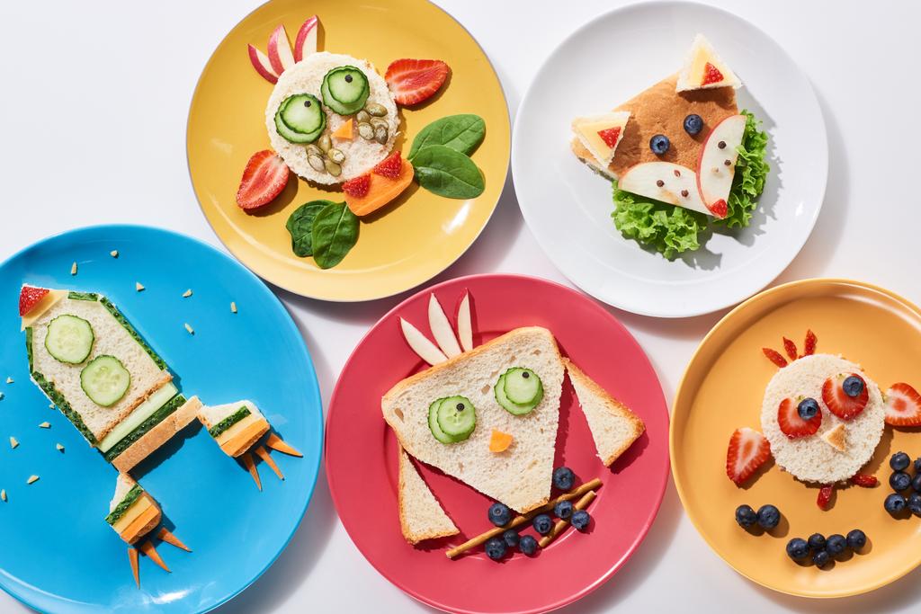 top view pf plates with fancy animals and rocket made of food for childrens breakfast on white background - Photo, Image