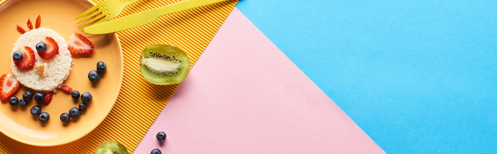 vista superior da placa com animal de fantasia feito de alimentos para crianças café da manhã perto de talheres em fundo azul, amarelo e rosa
 - Foto, Imagem