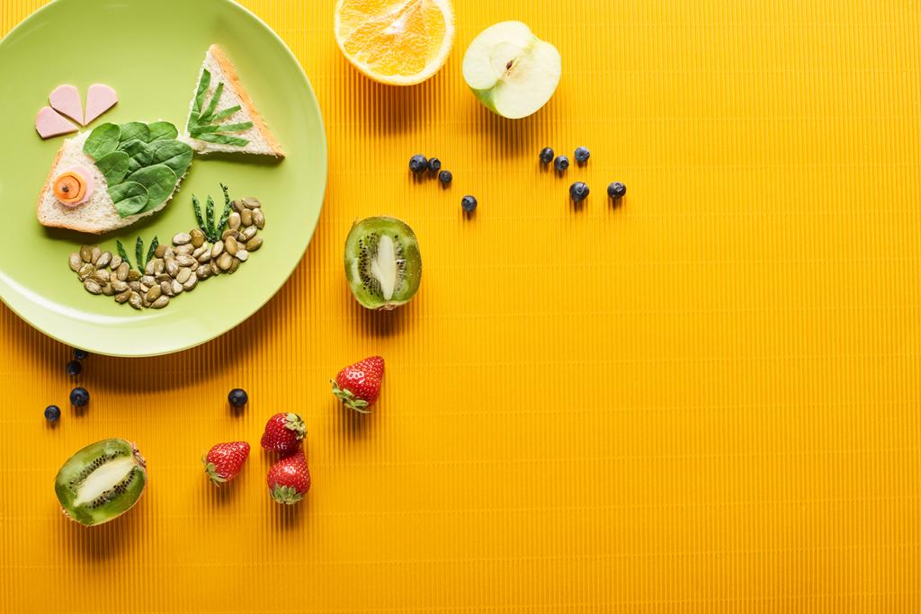 вид сверху на тарелку с модной рыбой из еды рядом с разбросанными фруктами на красочном оранжевом фоне
 - Фото, изображение