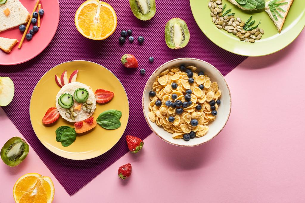 верхний вид тарелок с модными животными из продуктов питания рядом фруктов и завтрака хлопья на фиолетовом фоне
 - Фото, изображение