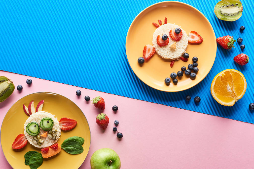 Top uitzicht op platen met fancy dieren gemaakt van voedsel op blauwe en roze achtergrond - Foto, afbeelding