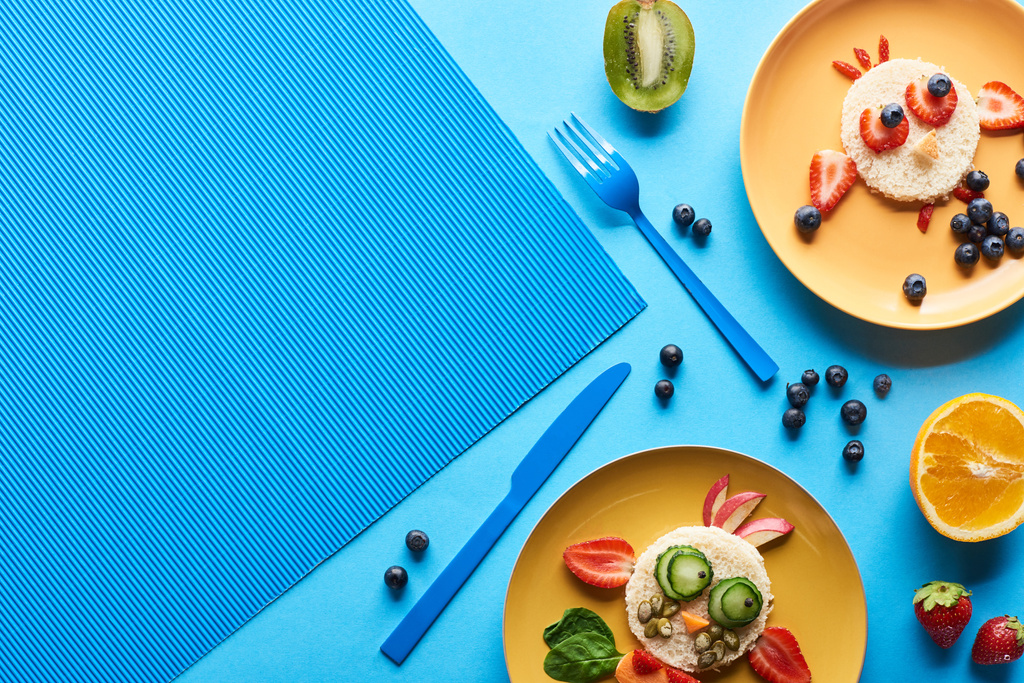 felülnézet tányérok kék háttérrel, élelmiszerből készült díszes állatokkal - Fotó, kép