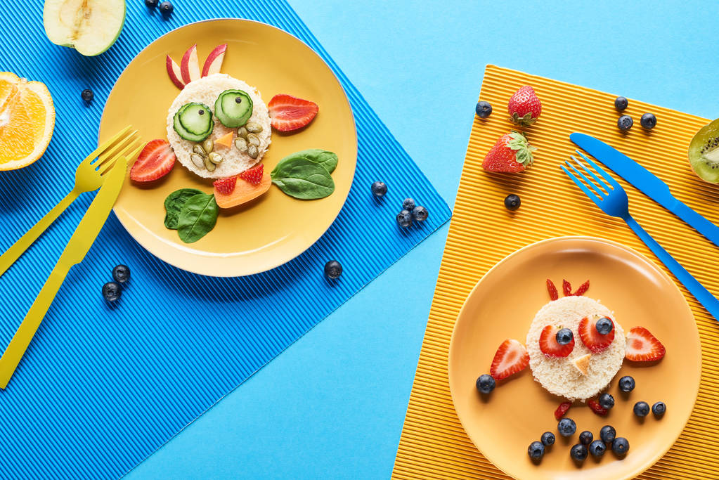 bovenaanzicht van platen met fancy dieren gemaakt van voedsel op de blauwe en gele achtergrond - Foto, afbeelding