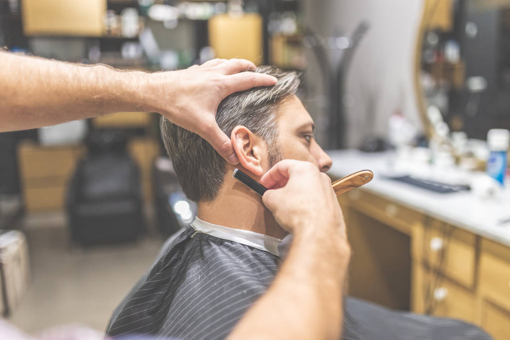 Hände des Friseurs halten Rasiermesser und rasieren einen Kunden. - Foto, Bild