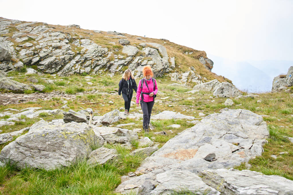 Дві жінки з рюкзаками ходять по гірській стежці
 - Фото, зображення