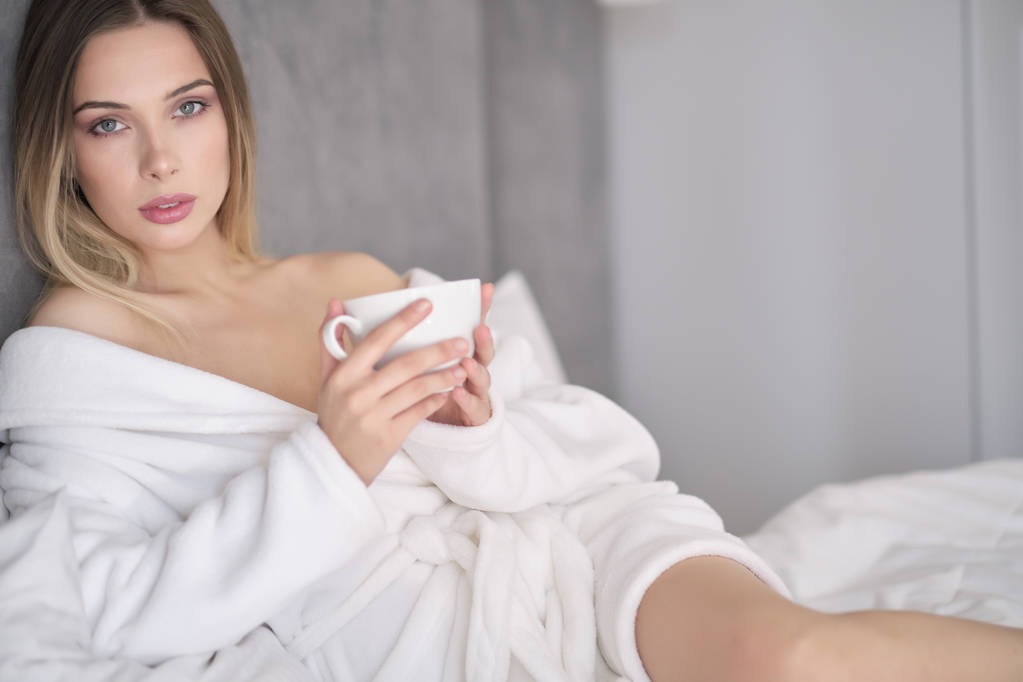 mujer en un albornoz bebe café de la mañana en la cama
 - Foto, imagen