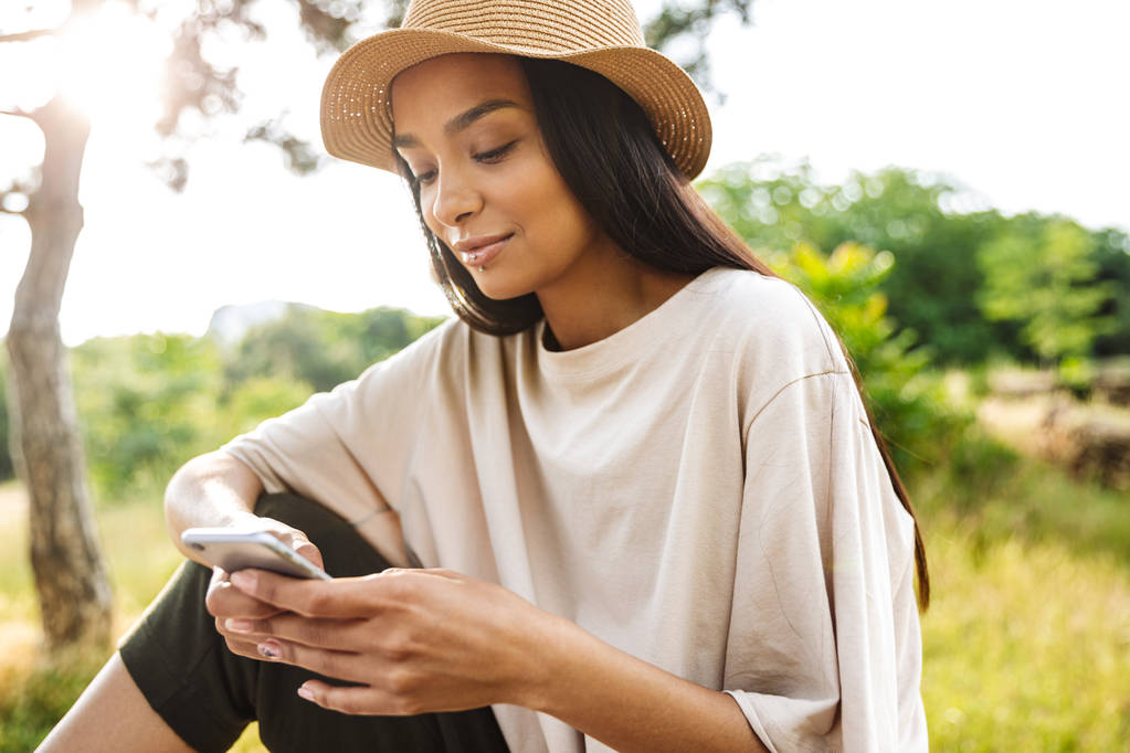 Ritratto di donna contenta con cappello di paglia che tiene lo smartphone seduta sulla panchina nel parco verde
 - Foto, immagini