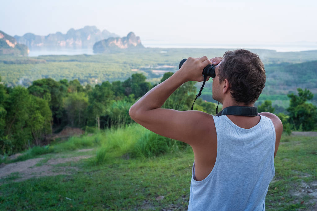 Een man kijkt door een verrekijker in de verte op de rotsen en het regenwoud - Foto, afbeelding