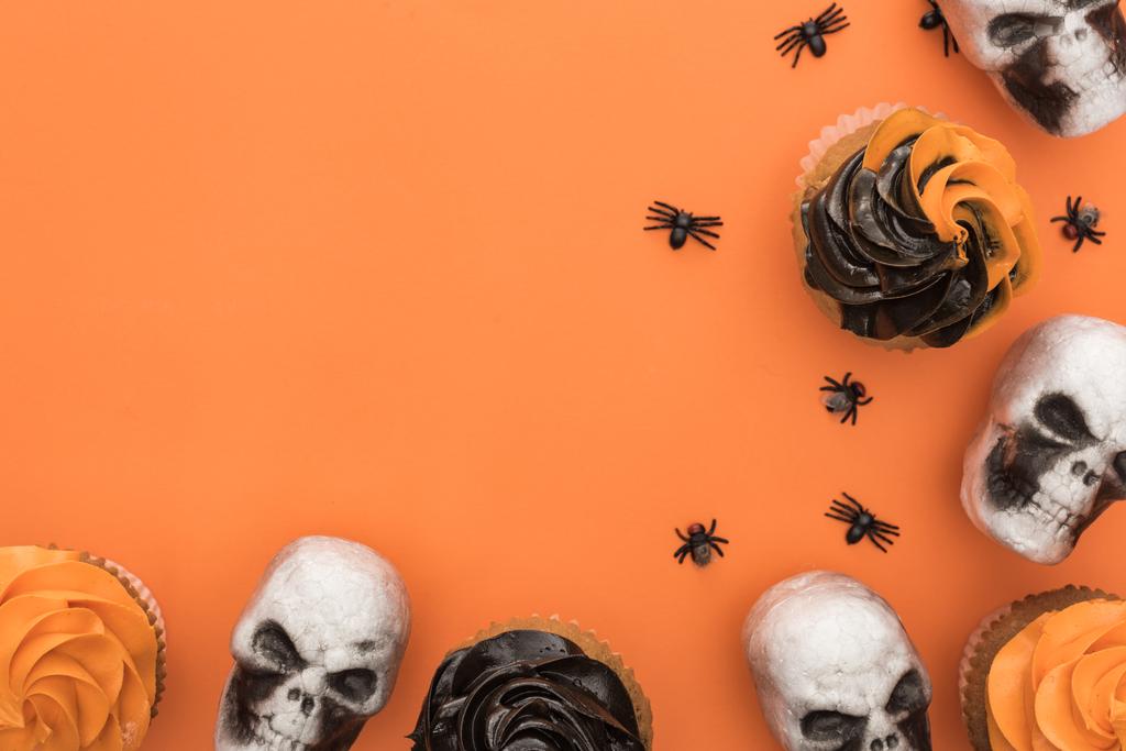 コピースペースとオレンジ色の背景にクモと頭蓋骨とハロウィーンカップケーキのトップビュー - 写真・画像