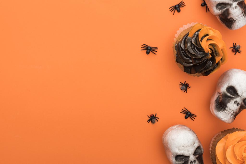 top view of tasty Halloween cupcakes with spiders and skulls on orange background with copy space - Photo, Image
